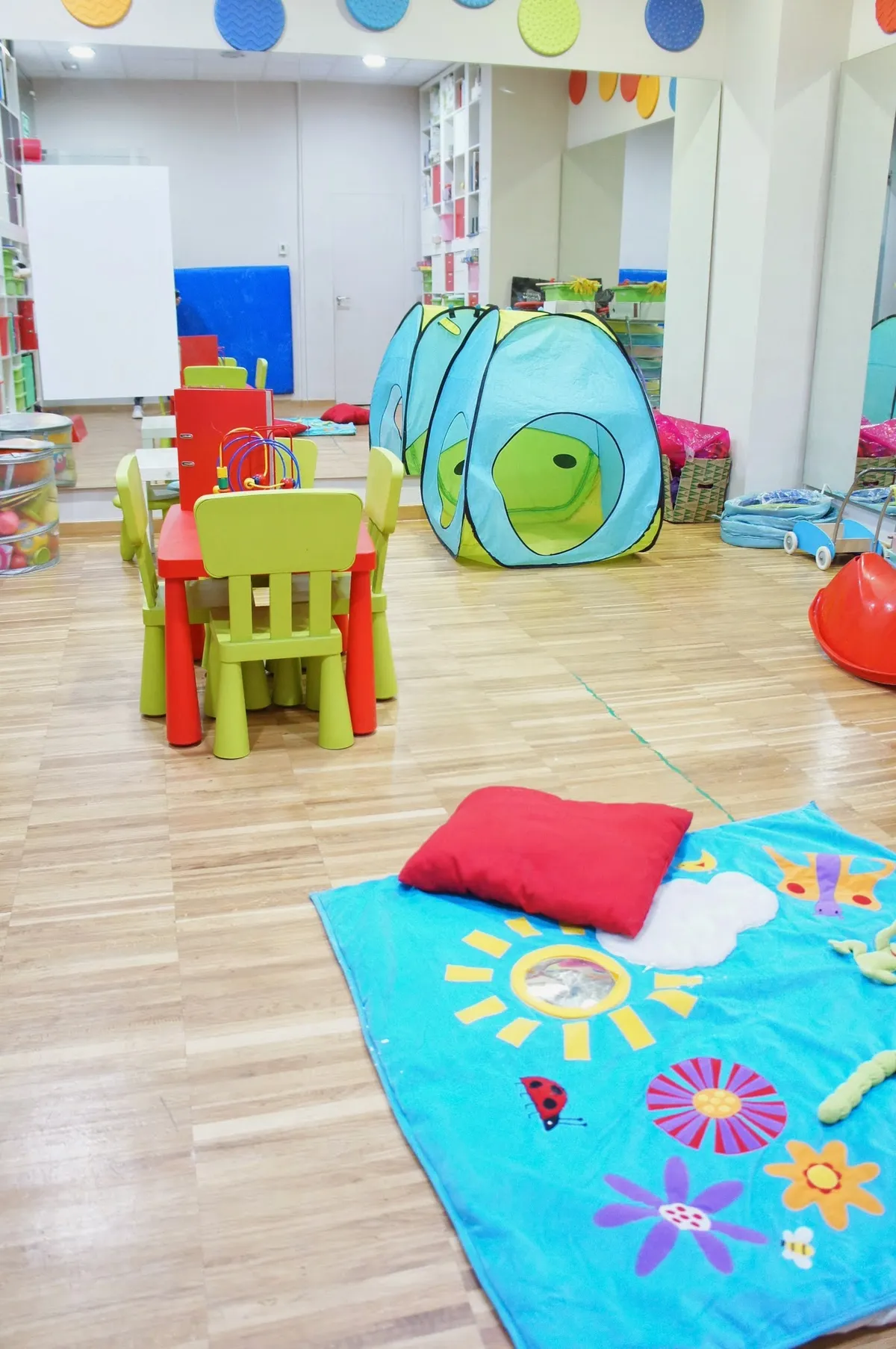 Sala de juego infantil del centro, con colchonetas, túneles y mesas de colores